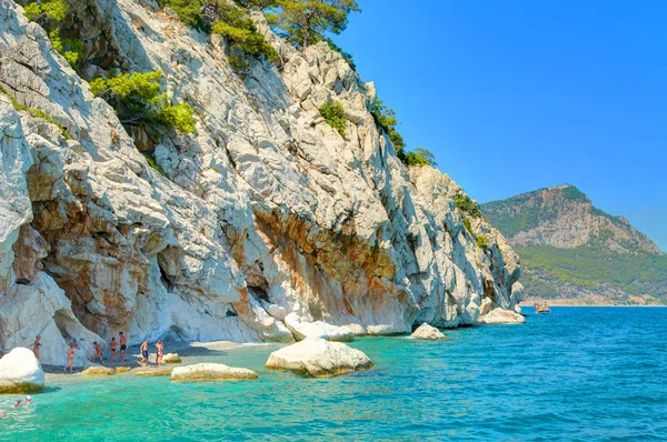 Пляж каменных пород песочного цвета с зелеными деревьями на побережье Средиземного моря Турции. Плавательный люди туристов. Лучшие Турция праздники отдых известные лодочные экскурсии на Средиземном море — стоковое фото